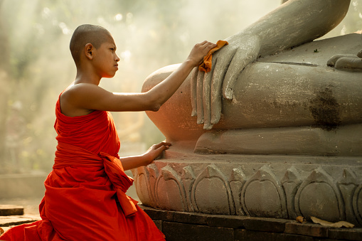 A novice monk uses a cloth to clean a large Buddha image.
