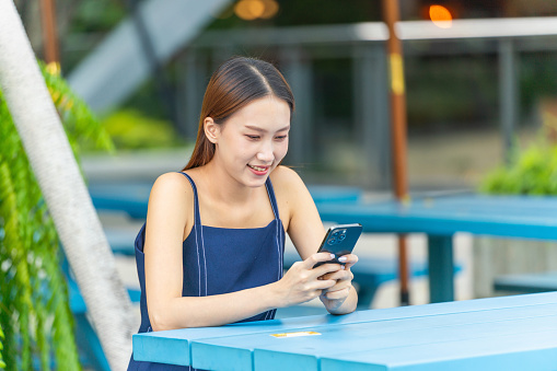Seamless Transactions: Asian Woman Conducting Digital Banking Credit Card Transaction on Phone at an Outdoor Park