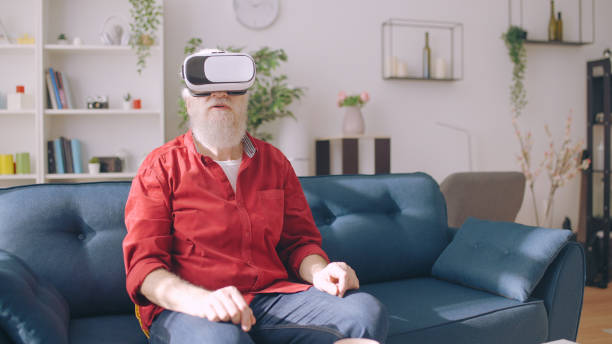 istock A senior man wears virtual reality glasses while seated on a sofa, exploring the world through a VR headset 1934345385