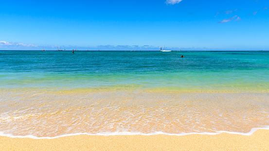 Colourful shore of a tropical beach. The sand is golden yellow, and the sea id a clear aqua blue. The beach is Waikiki beach, Hawaii