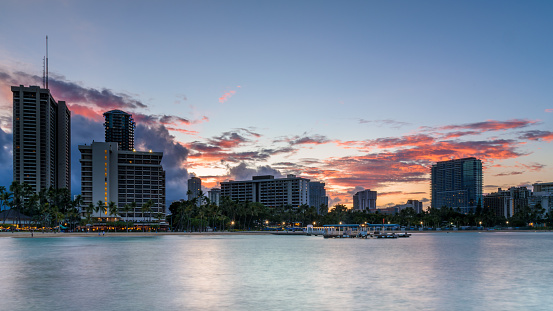 View of Waikiki beach skyline, at dawn on a summer's day. The sky is red, as the sun rises behind the buildings