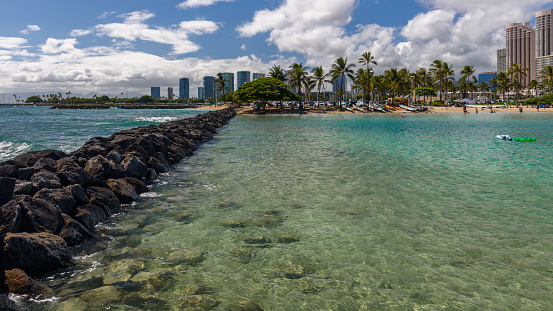 View towards a tropical beach, along a breakwater. The beach is Waikiki beach, in Honolulu, Hawaii
