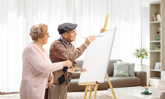 Senior man and woman painting with brushes on a canvas at home