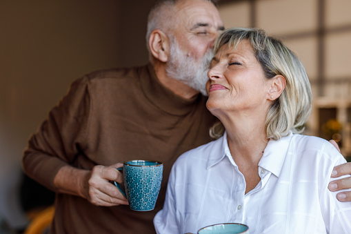 Portrait of happy mature woman smiling with eyes closed while enjoying a romantic kiss from her loving husband.
