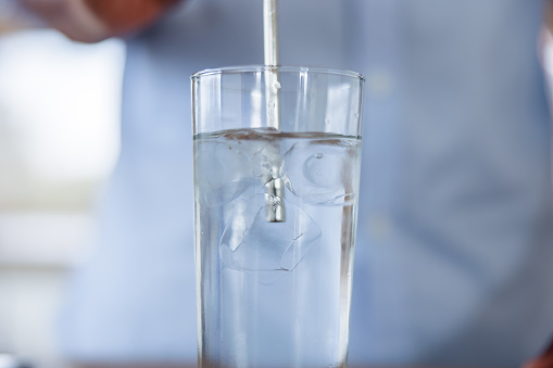 Close-up view of a scientist pouring a liquid into a glass of water as part of an experiment in a laboratory setting.