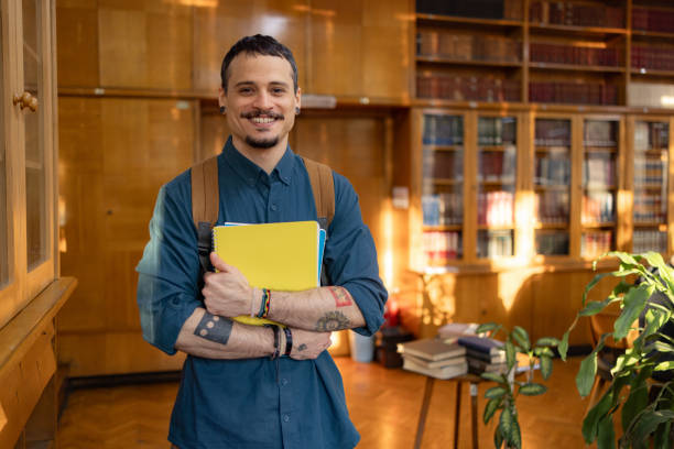 istock Happy male student holding books in a library. 1934387077