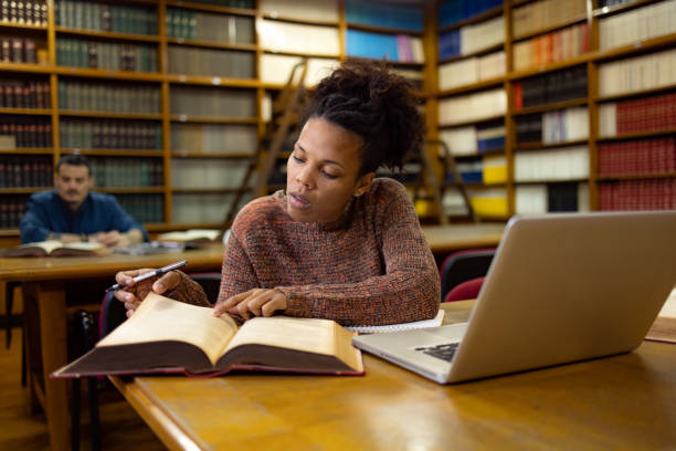 istock Black female college student learning from a book in a library. 1934388663
