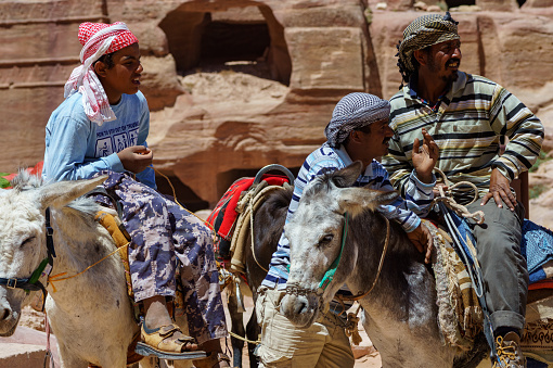 Jordan. Group of Bedouins wearing headdresses called Arafatka ride on donkeys to transport tourists around Petra. Ancient city of Petra, carved into rocks. Petra, Jordan – May 19, 2011