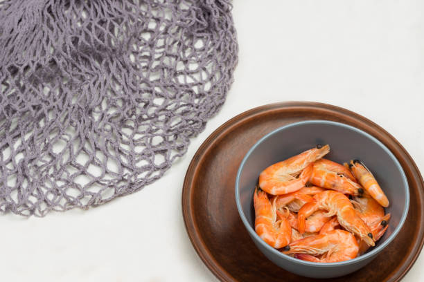 Shrimp in gray bowl. Gray mesh, allspice and lemon on table. White background. Top view