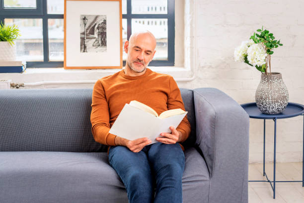 Mid aged man wearing casual clothes and relaxing on the sofa. Confident male wearing casual clothes and reading a book at home.