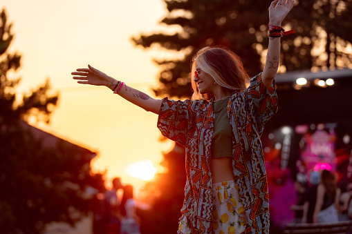 Young happy woman having fun while dancing on an outdoor music festival at sunset.