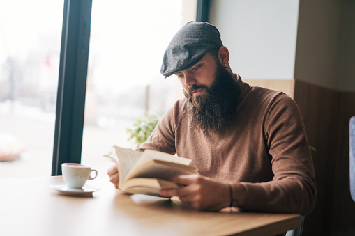 Young handsome man reading book in a modern cafe restaurant