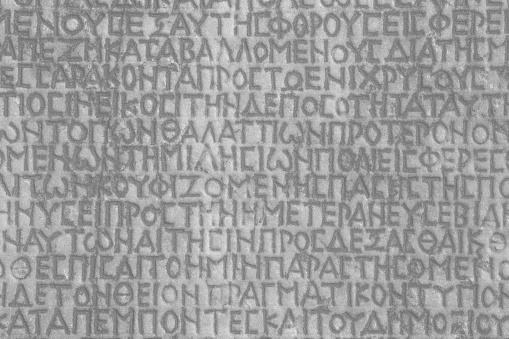 Retro text background. Fragment of ancient inscription (imperial law in ancient Greek language), carved on marble block. Monochrome. Ancient Miletus, Turkey (Turkiye). Ancient art and history concept