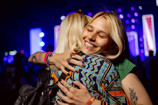 Happy woman greeting her friend with a hug on a music concert at night.
