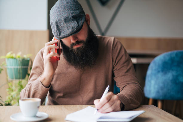 istock Focused bearded  freelancer writing in notebook and talking on the phone 1934434140