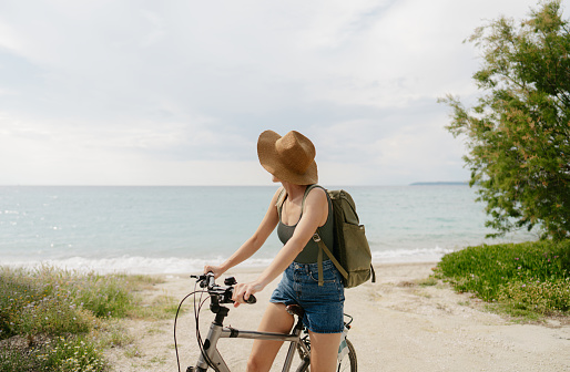 Photo of a young woman riding a bicycle by the sea on a summer day
