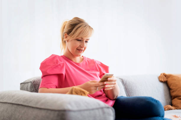 istock Blond haired mature woman sitting at home and text messaging 1934441515