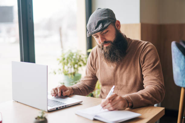 istock Shot of a young man using his laptop while sitting by the window in a cafe 1934441527