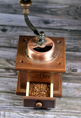 a manual coffee grinder burr mill machine with catch drawer, conical burr mill and spice hand grinding, an old style classic vintage retro coffee beans grinder with a wood drawer with coffee inside, selective focus