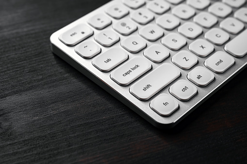 White aluminum computer keyboard on dark wooden office desk, selective focus