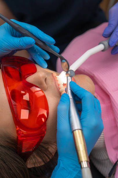 close-up dentist uses a drill and a dental mirror to treat the teeth of a young female patient in protective glasses. concept of dental hygiene and health. vertical photo - dental hygiene dental equipment dental drill practicing photos et images de collection