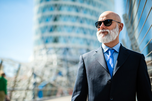 Mature bald stylish business man portrait with a white beard outdoor wearing sunglasses