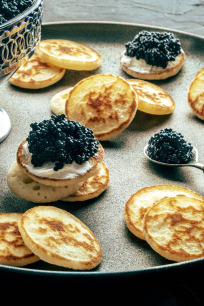 istock Blinis with black caviar, on a festive dish on a black background, mini pancakes 1934472429