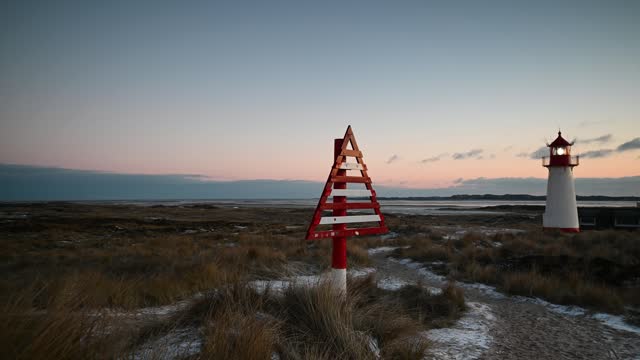 Footage of lighthouse List West and red-white triangular, wooden directional signs (border beacon) serving as day markers at evening in winter landscape.Sylt, Lighthouse Ellenbogen, Northernmost point