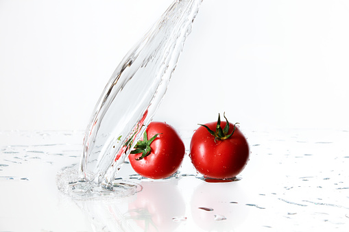 Two fresh tomatoes with water splash on white background. Selective focus.