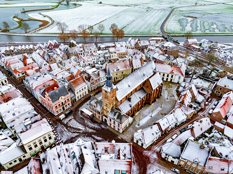 Hattem aerial view during a cold winter morning with snow on the rooftops seen from above. The town Hattem is bordering the forests of ‘De Veluwe’ on one side and lies along the IJssel river the other side, which can be seen in the background.