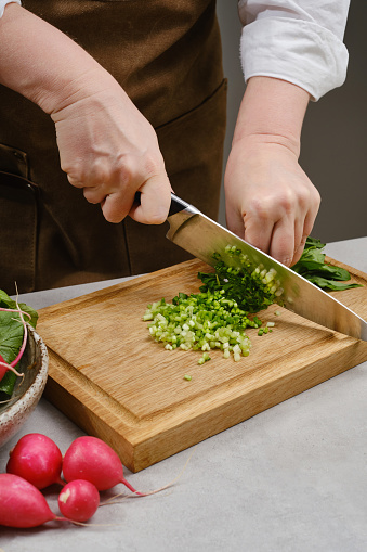 The chef cuts wild garlic on a wooden board with a knife. Chef preparing salad with vegetables, cut vegetables. Healthy and tasty nutrition. Cooking and home recipes. Shallow depth of field