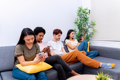 Group of young adults using smartphones on a couch in a home setting.