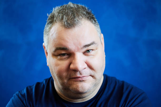 istock Piercing glance from under his brows, European man, 47 years old,  stares with his head slightly lowered, his face close up on blue background. 1934520431