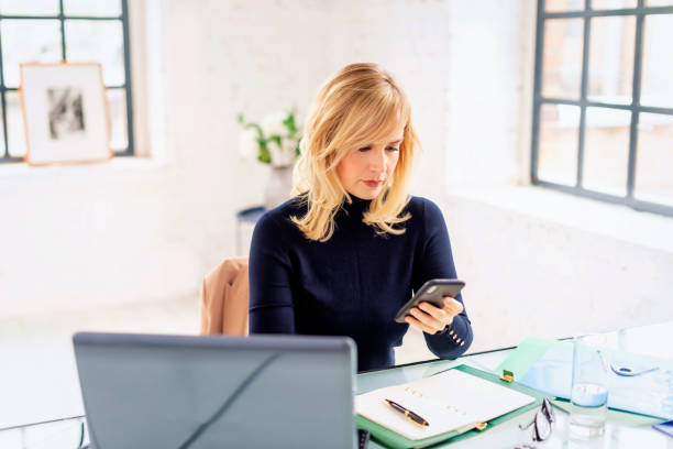 istock Mid aged blond haired woman sitting at desk and using laptop for work 1934528047