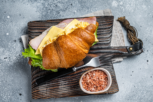 Croissant sandwich with turkey ham, scrambled eggs, cheese and lettuce salad. Gray background. Top view.