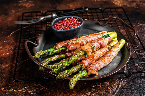 Baked Prosciutto wrapped green asparagus. Dark background. Top view.