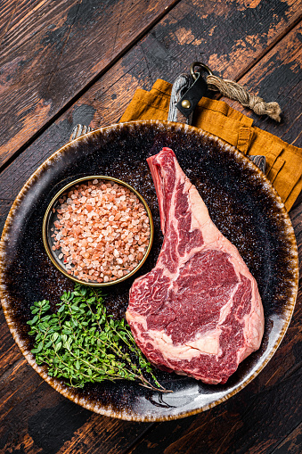 Raw prime cowboy or rib eye steak, dry aged beef meat. Wooden background. Top view.