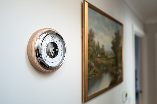 Shallow focus of a high precision, classic style weather pressure barometer seen in the hallway of a new home. The barometer is used to give advance notice of a change in weather conditions.