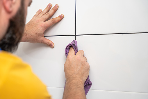 Man wipes tile joints after painting it with black acrylic marker