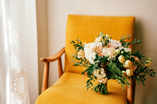 Bride bouquet stands in a yellow chair in a hotel room. High quality photo