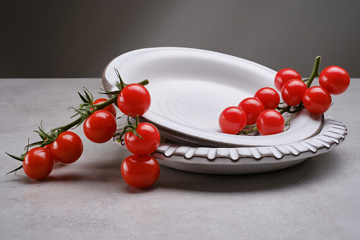 Red cherry tomatoes in a white porcelain bowl on the gray granite table. Sprig of cherry tomatoes on a gray concrete background. Selective focus
