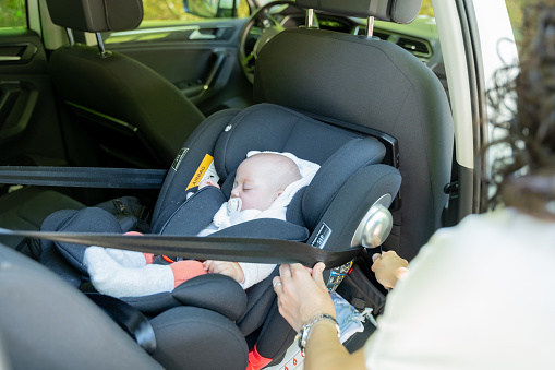 young mother adjusting the seat belt of her baby's transport seat in the car, child restraint system in the vehicle. safety concept in child transportation