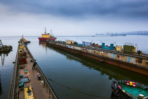 istock Icebreaker ship navigates into floating dock for maintenance at shipyard, surrounded by tugboats under overcast sky, showcasing maritime industry and vessel refurbishment. 1934580750