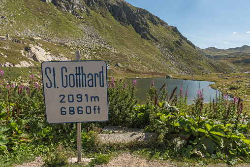 Mountain lake at Gotthard Pass. In the foreground a place-name sign with altitude indication.