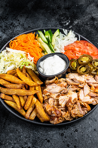 Shawarma Doner kebab on a plate with french fries and salad. Black background. Top view.