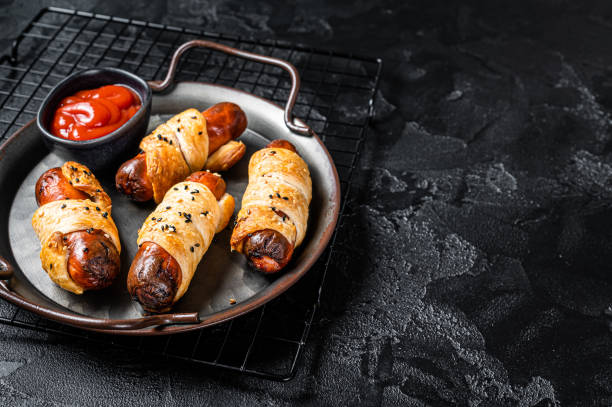 pigs in blanket puff pastry sausage wrap roll. black background. top view. copy space - blanket pig hot dog sausage stock-fotos und bilder