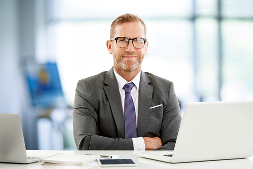 Middle aged sales director businessman sitting at desk and working on laptop. Professional man wearing suit and eyeglasses.