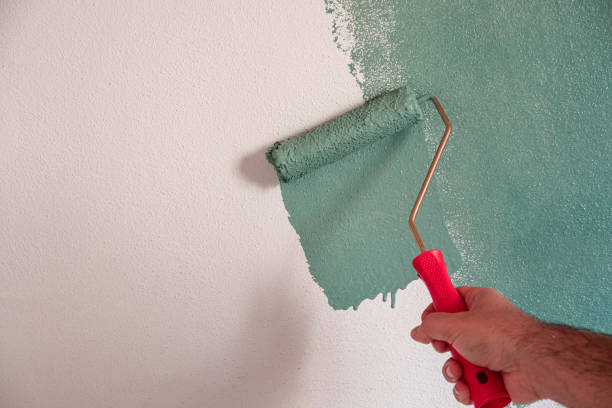 istock Repairman painting white wall in apartment green using roller, closeup 1934630547