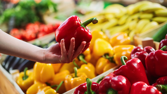 Woman Buying Fresh Vegetables from a Local Farm Market Stall. Close Up Footage Focusing on a Female Hand Choosing a Ripe Red Bell Pepper from a Selection on a Stand with Natural Produce
