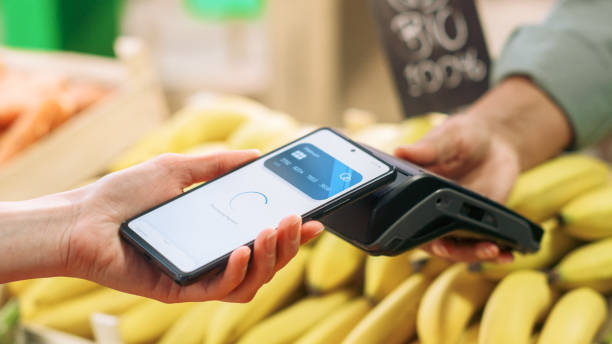 istock Close Up of a Customer Making a Secure Swift Contactless Payment Using a Smartphone with a Credit Card Banking NFC App. Modern Shopper Buying Organic Fruits and Vegetables From a Farm Market Stall 1934644598